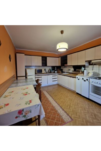 A kitchen in a family house with a wooden decor floor and a decorative tablecloth on the table.