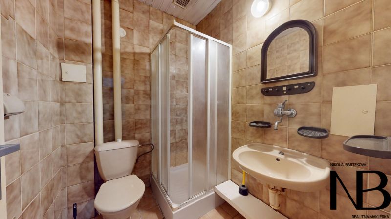 A bathroom in a studio apartment with a toilet, sink, and shower, tiled.