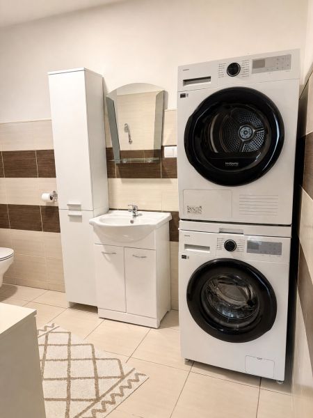 Washing machine and dryer in the bathroom of a family house with marble tiles and a mirror.