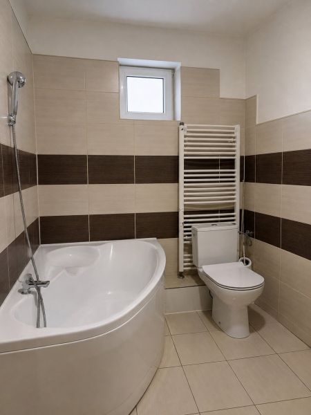 A bathroom in a family house with a bathtub, toilet, and radiator, tiles with a brown decor.