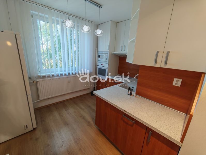 A kitchen in a studio apartment with a wood-patterned floor and natural light.