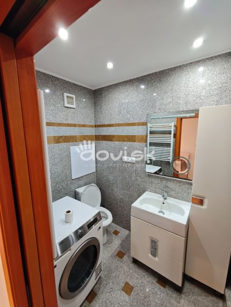 Bathroom in a studio apartment with a sink, toilet, washing machine, and light-colored walls.