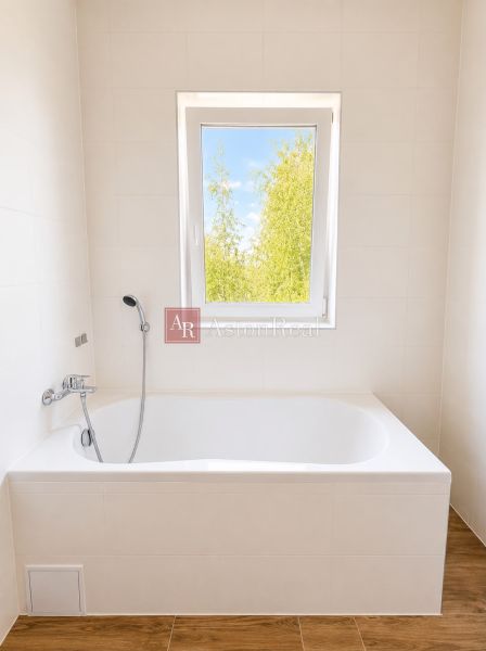 Bathroom with a bathtub and a window, white tiles, floor with wood decor in a 3-room apartment.