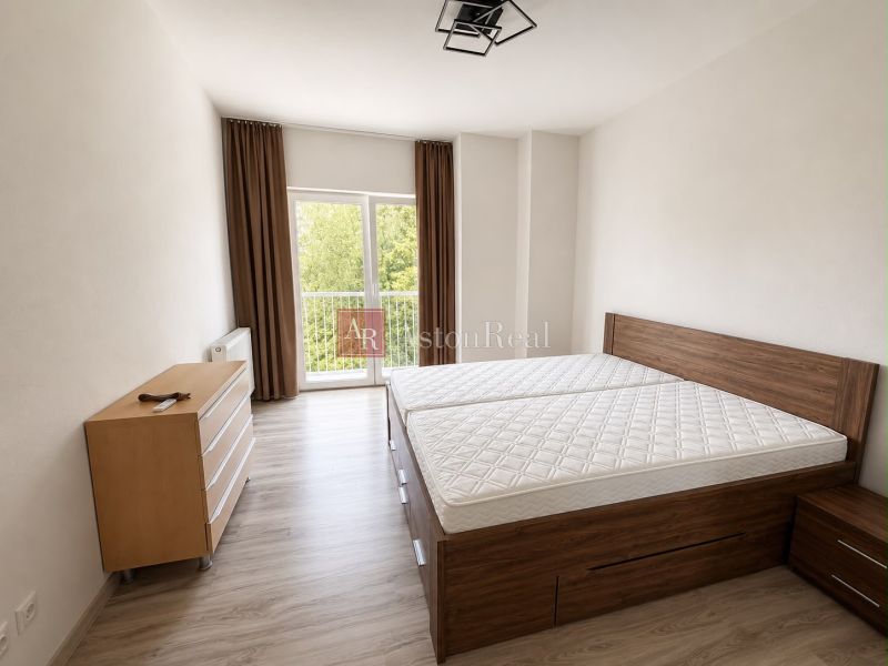 Bedroom with light walls, wood-patterned flooring, a large bed, and a dresser.