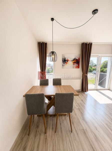 Dining area in a 3-room apartment with a wood-patterned floor and a large window.
