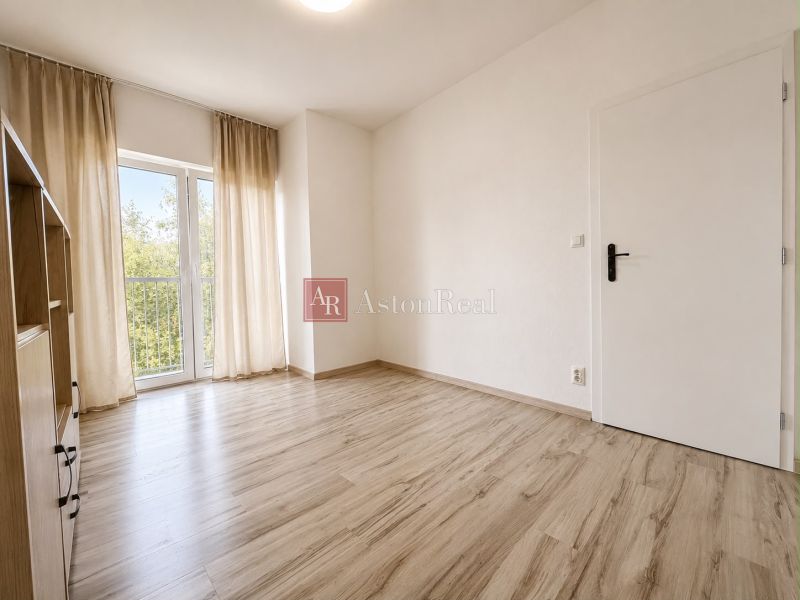 A bright room with a wood-patterned floor and curtains in a three-room apartment.