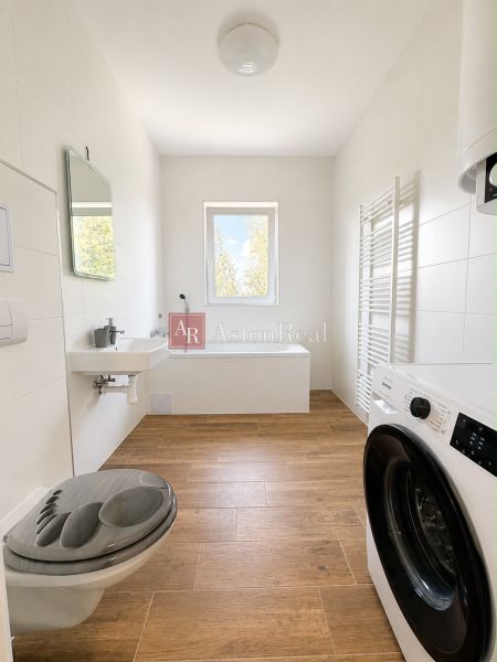 A bathroom in a 3-room apartment with a bathtub, washing machine, and a floor with a wooden decor.