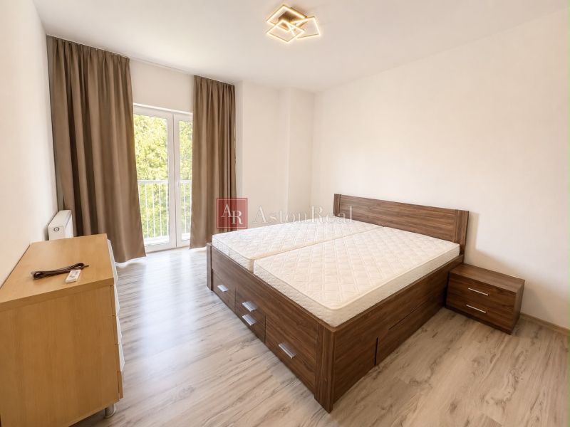 A bright bedroom with a bed, a nightstand, and a wooden decor floor in a 3-room apartment.