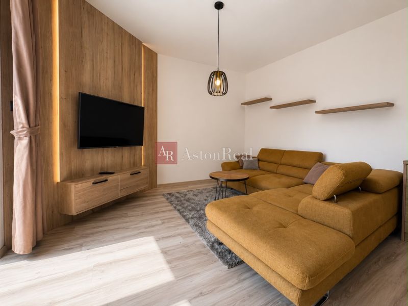 Living room in a 3-room apartment with a sofa, wooden decor flooring, and a TV on the wall.