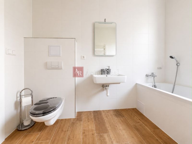 A bathroom in a 3-room apartment with a bathtub, toilet, and a floor with a wooden decor.
