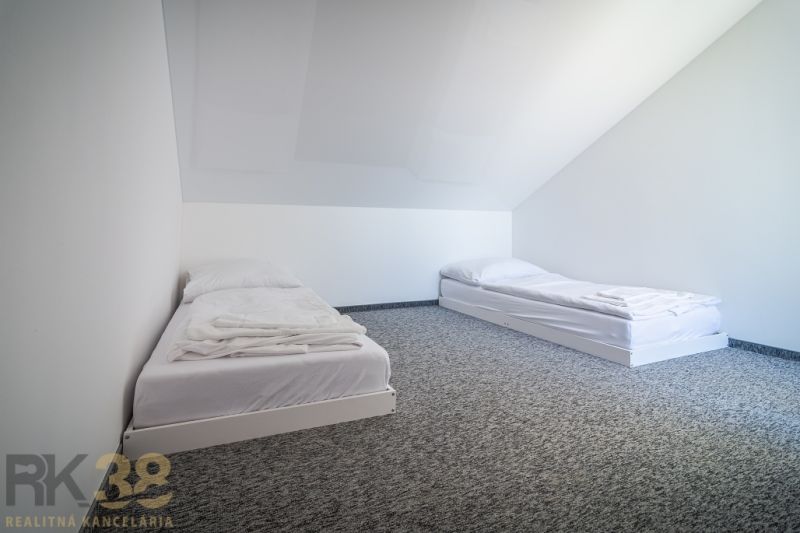 Two beds in the attic of the Holiday Apartment with smooth white walls and carpeted floor.