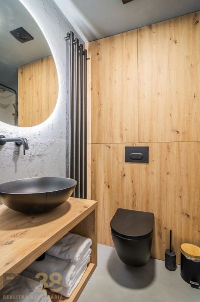 Bathroom in a holiday apartment with a black sink and a wall with a wooden decor.