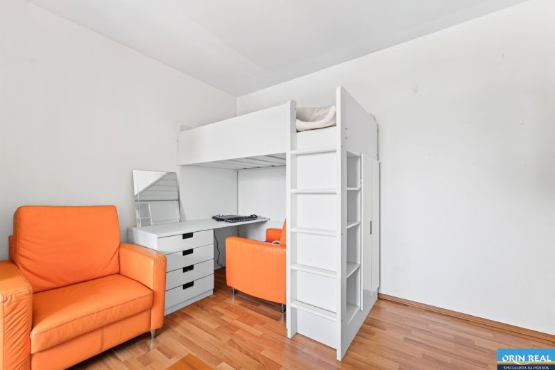 Children's room in a three-room apartment with a wooden decor floor and an orange armchair.