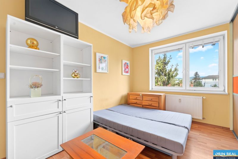 A bright room with a bed, shelves, and a floor with a wooden decor in a 3-room apartment.