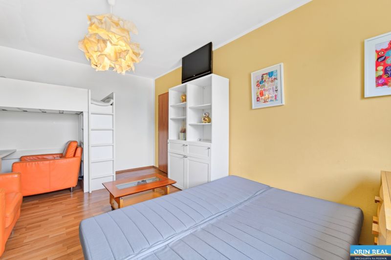A sofa bed, a bunk bed, an orange armchair, and a wooden decor floor in a 3-room apartment.