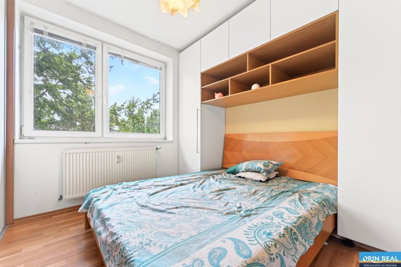 A bedroom in a 3-room apartment with a bed, storage space, and a floor with a wooden decor.