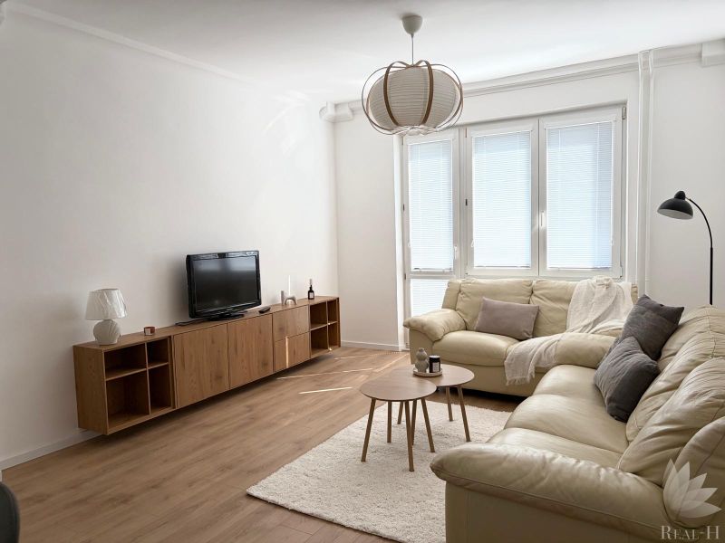 A bright living room of a 3-room apartment with sofas, a TV, and a wooden-decor floor.