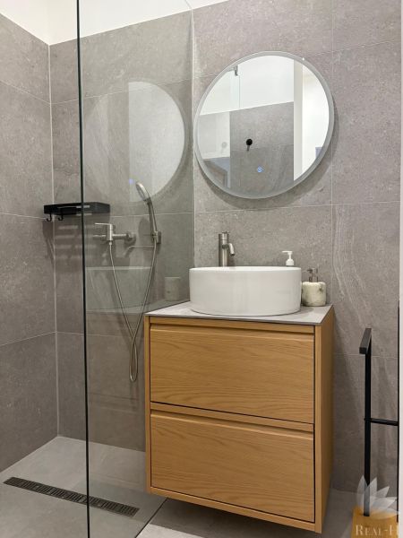 Bathroom with a shower, mirror, sink, and cabinet in a 3-room apartment.