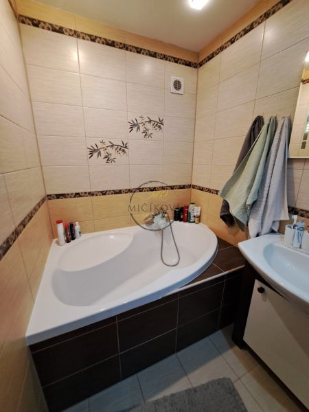 A bathroom with a corner bathtub and subtle tiles in a 3-room apartment.
