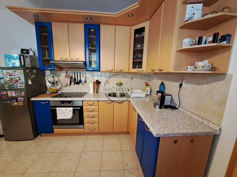 A kitchen of a three-room apartment with a wooden decor and blue kitchen cabinets.