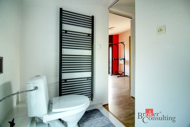 Bathroom with a toilet, radiator, and a view into the gym in a family house.