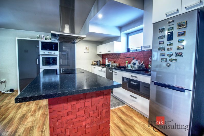 A kitchen in a family house with an island, red tiles, and a wooden decor floor.