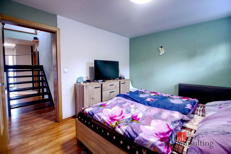 A bedroom in a family house with a television, a dresser, and a bed with floral bedding.
