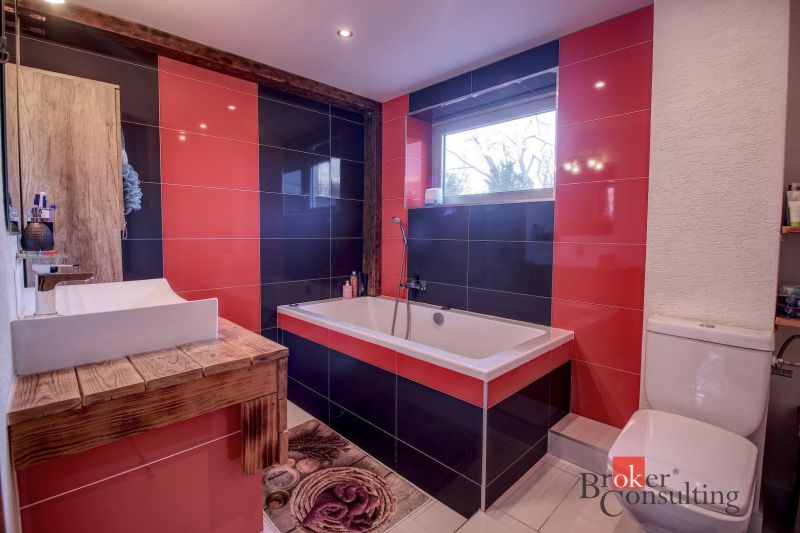 Bathroom with red and black tiles, a bathtub, and a wooden sink table in a family house.