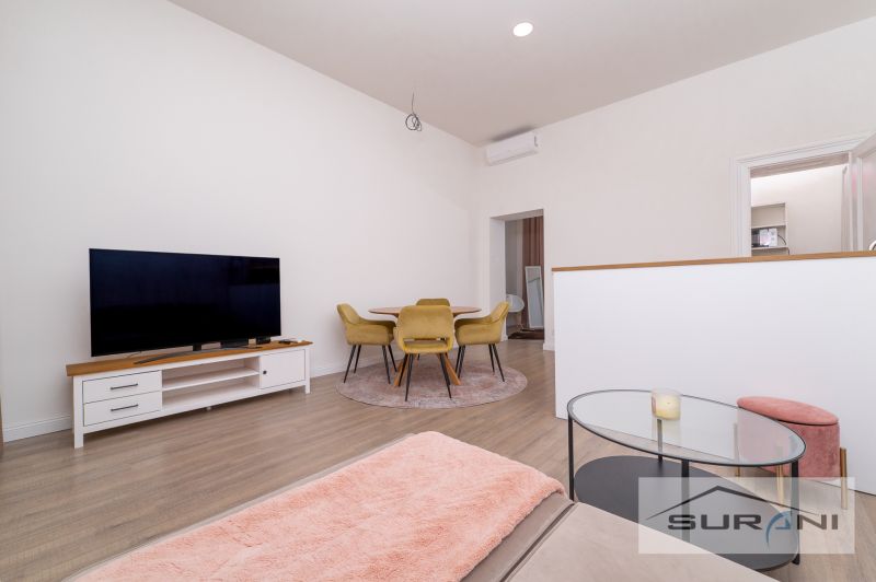 Living room in a 2-room apartment with a television, couch, and wooden decor flooring.