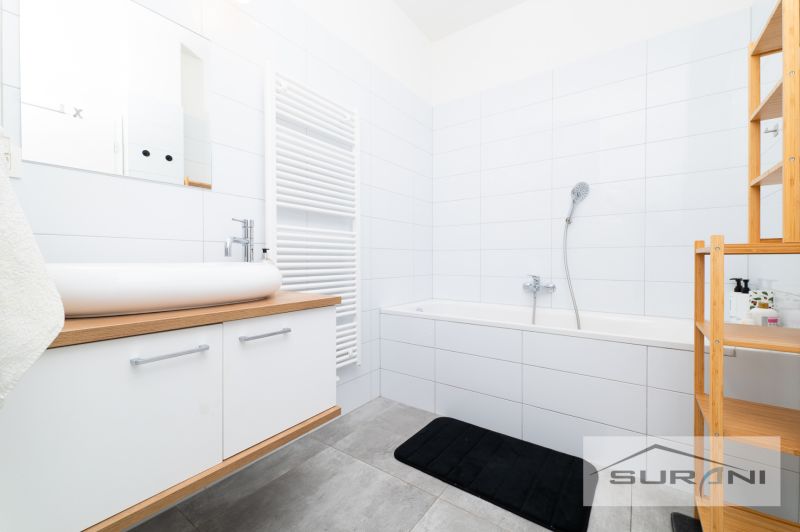 Bathroom in a 2-room apartment with a bathtub, sink, cabinet, and shelving unit.