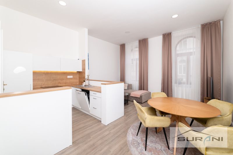 A kitchen in a 2-room apartment with a wood-patterned floor, a dining table, and windows with curtains.