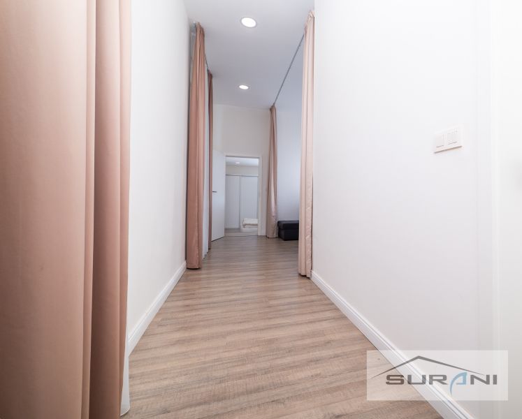A hallway with a wooden decor floor, white walls, and light pink curtains in a 2-room apartment.