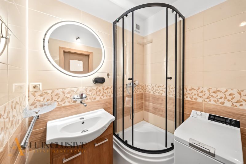 A bathroom in a 2-room apartment with a shower, sink, and washing machine.
