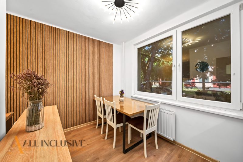Dining area with a table, chairs, wooden wall, and floor with a wooden decor in a 2-room apartment.