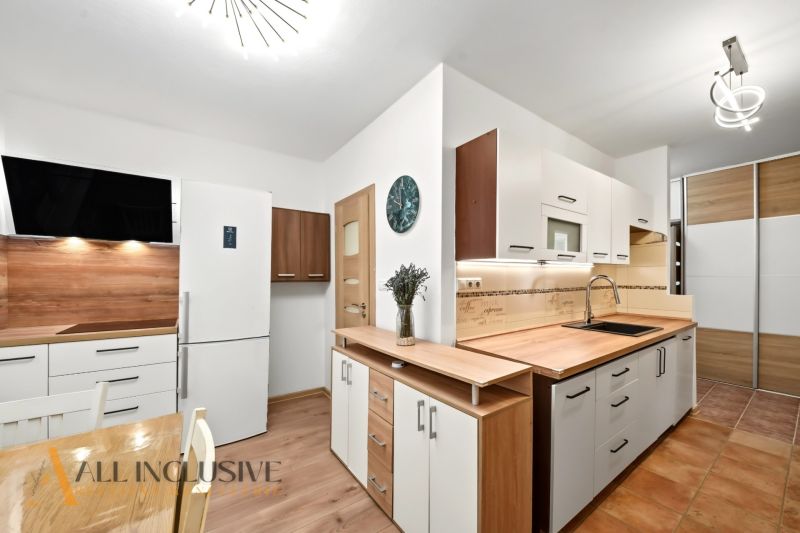 A kitchen in a 2-room apartment with a white refrigerator, wooden decor on the floor and walls.