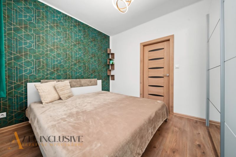 A bedroom with green geometric wallpaper, a bed, and a wooden decor floor in a two-room apartment.