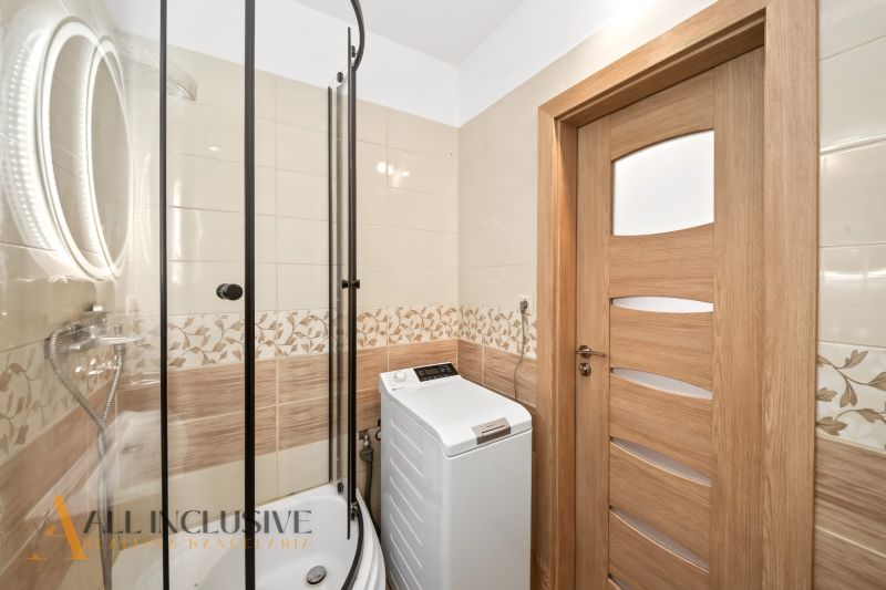 Shower corner and washing machine in the bathroom of a 2-room apartment with wooden floor decor.