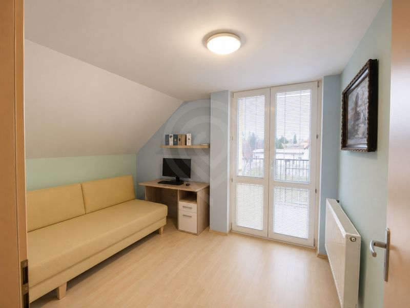 A room with a sofa, a computer desk, and a wooden-patterned floor in a family house.