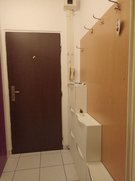Entrance hallway in a one-room apartment with a coat rack, white cabinets, and tiles.