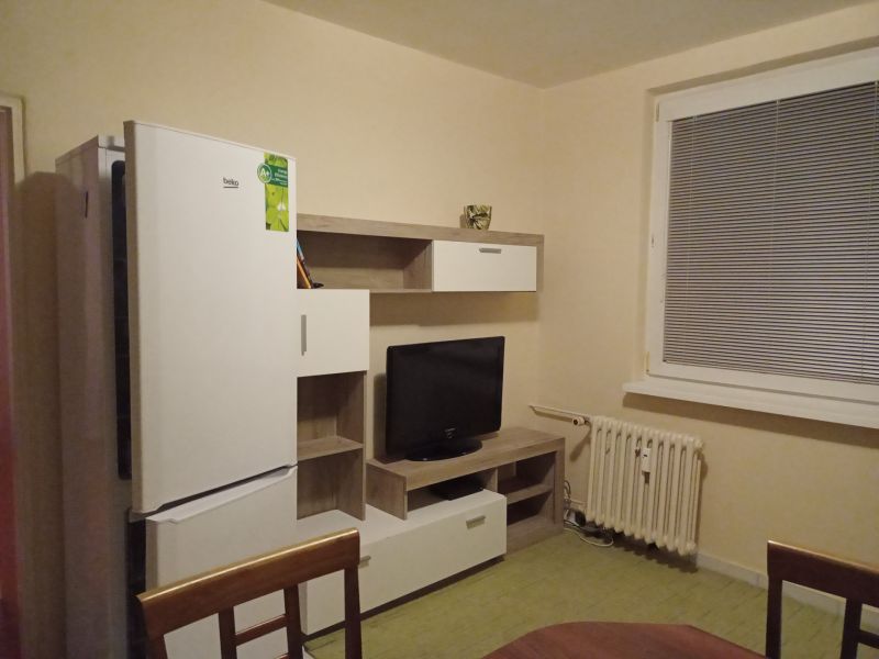 A kitchen in a furnished studio apartment with a refrigerator and a television.