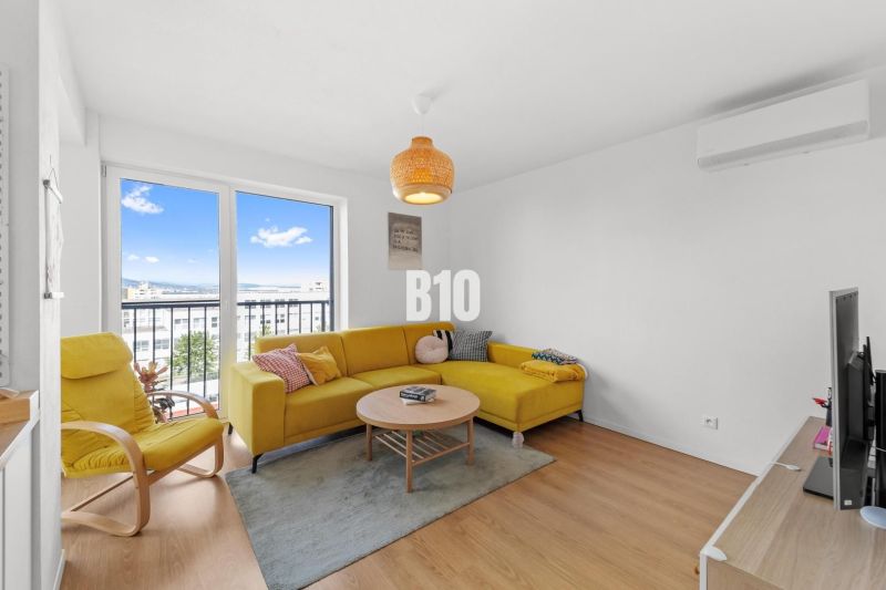 Living room of a 4-room apartment with a yellow sofa and a large window, floor with wooden decor.