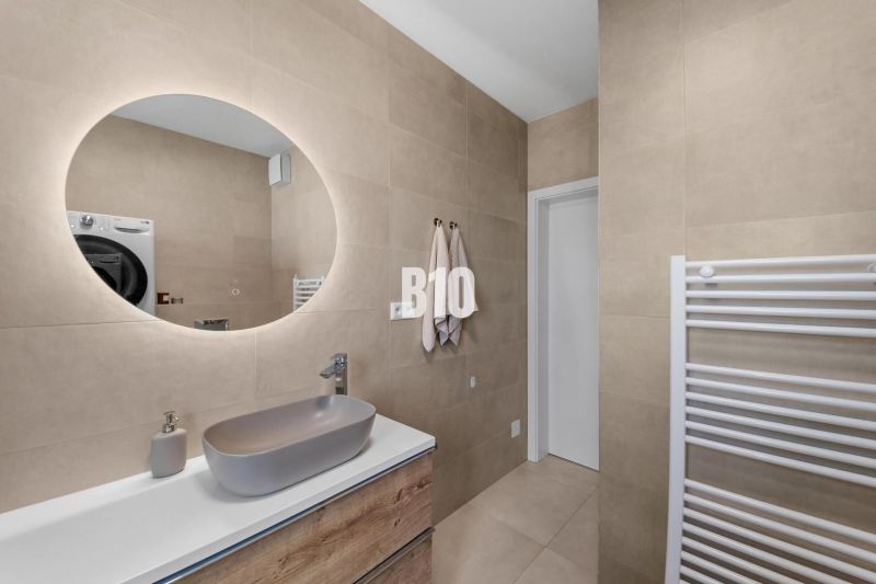 A bathroom in a 4-room apartment with a round mirror and a sink on beige walls.