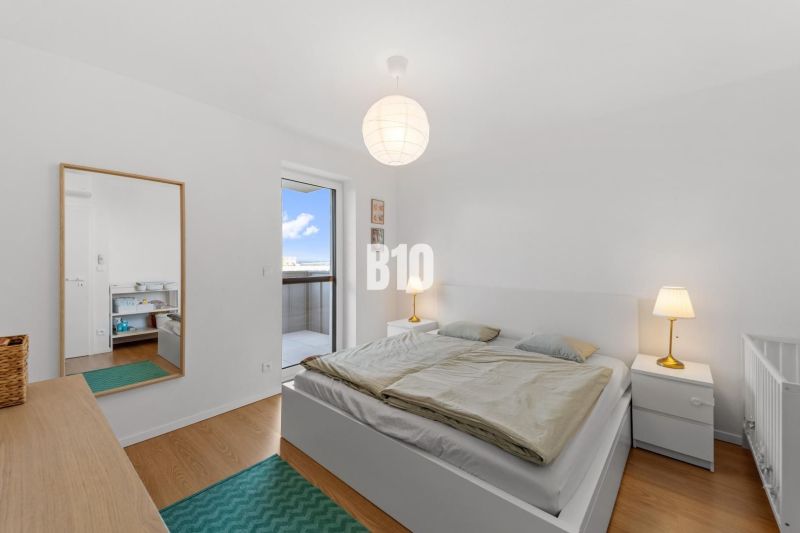 A bright bedroom with wood-patterned flooring and access to a balcony in a 4-room apartment.