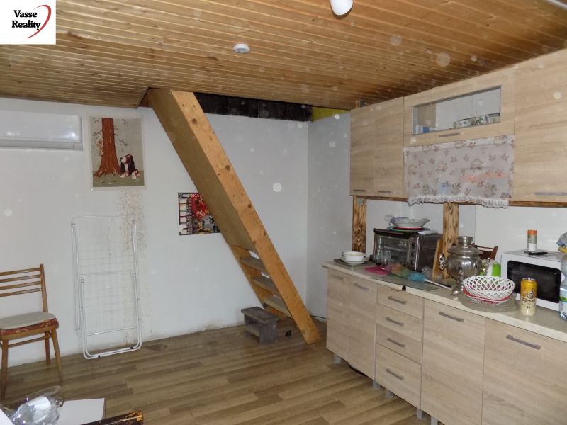 The interior of the cottage with stairs, a kitchen unit, and a wooden decor floor.
