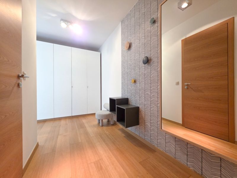 Interior of a 1-room apartment with a wood-patterned floor, a white wardrobe, and a mirror.