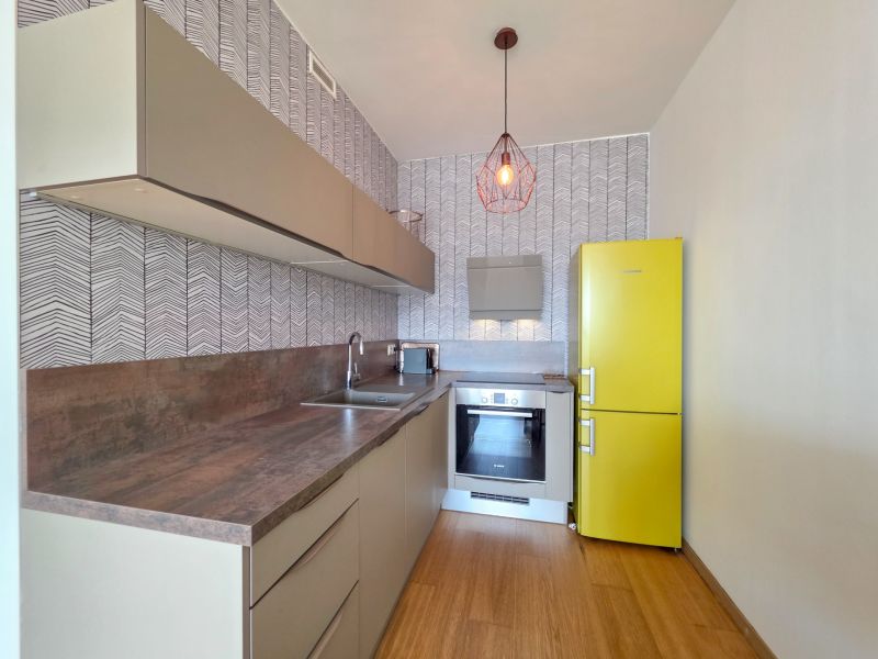 A kitchen in a studio apartment with a yellow refrigerator and a wood-patterned floor.