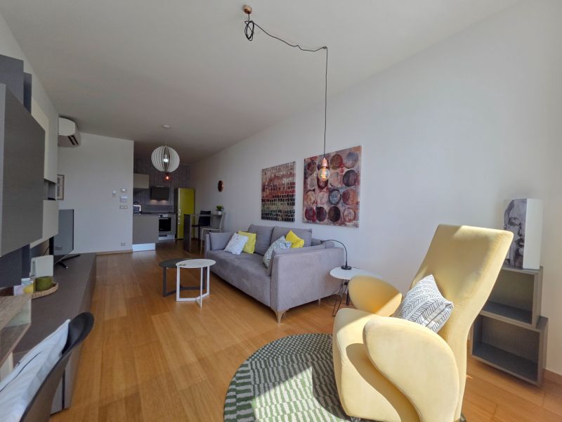 Living room with wood-patterned flooring, a sofa, and a cream armchair in a studio apartment.