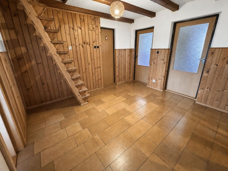 Interior of a family house with wooden paneling, staircase, and ceramic flooring.