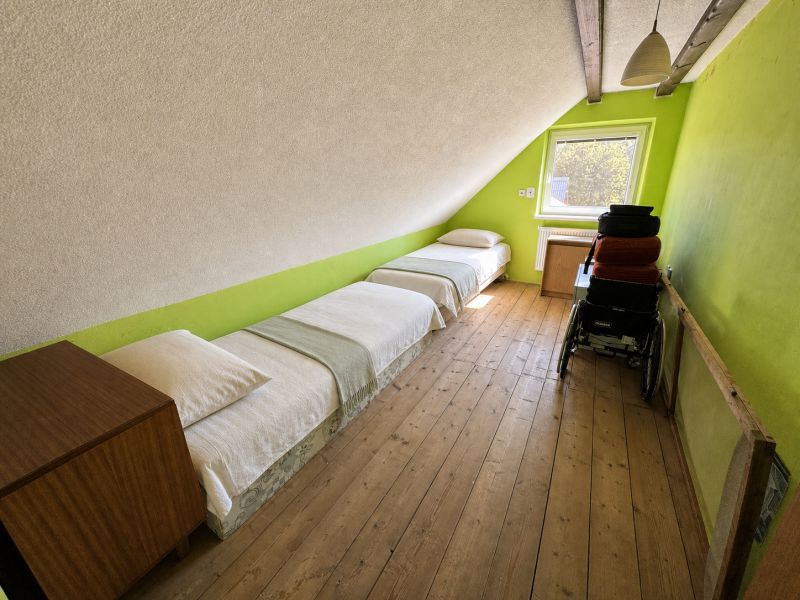 Attic room in a family house with two beds, wooden floor decor, and a cart.