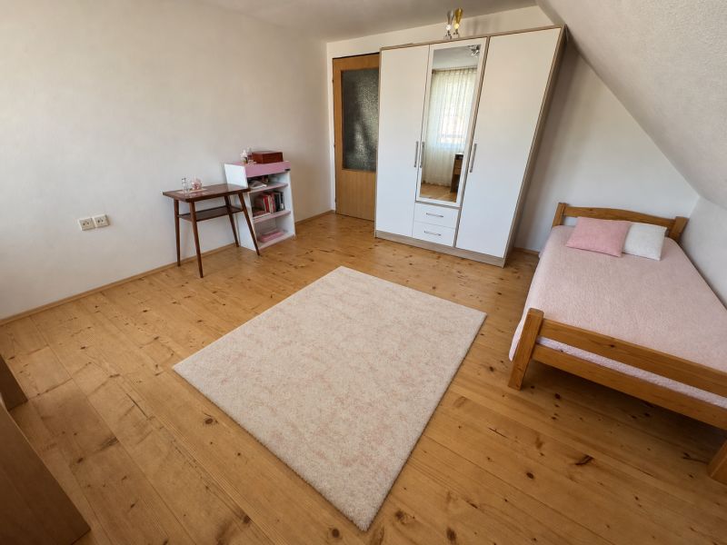 A room in a family house with a bed, a wardrobe, and a floor with a wooden decor.